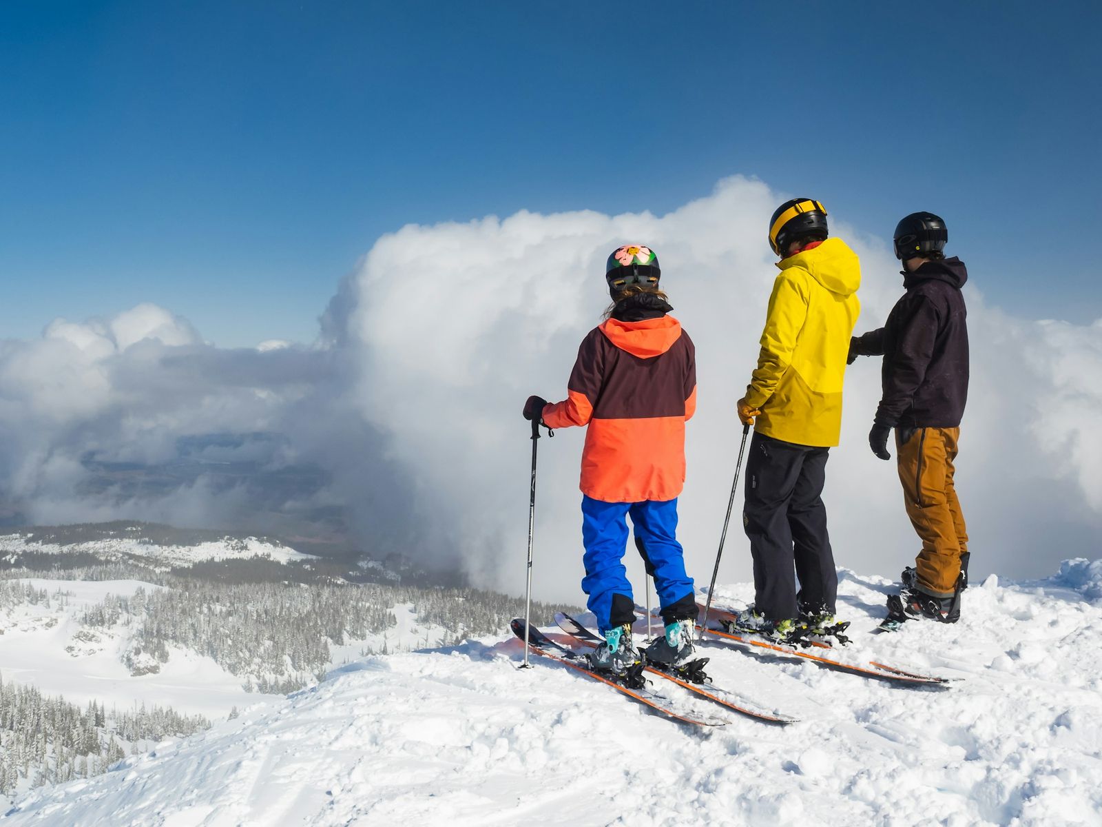 Three friends with skis standing at the edge of a ridge above a sea of clouds