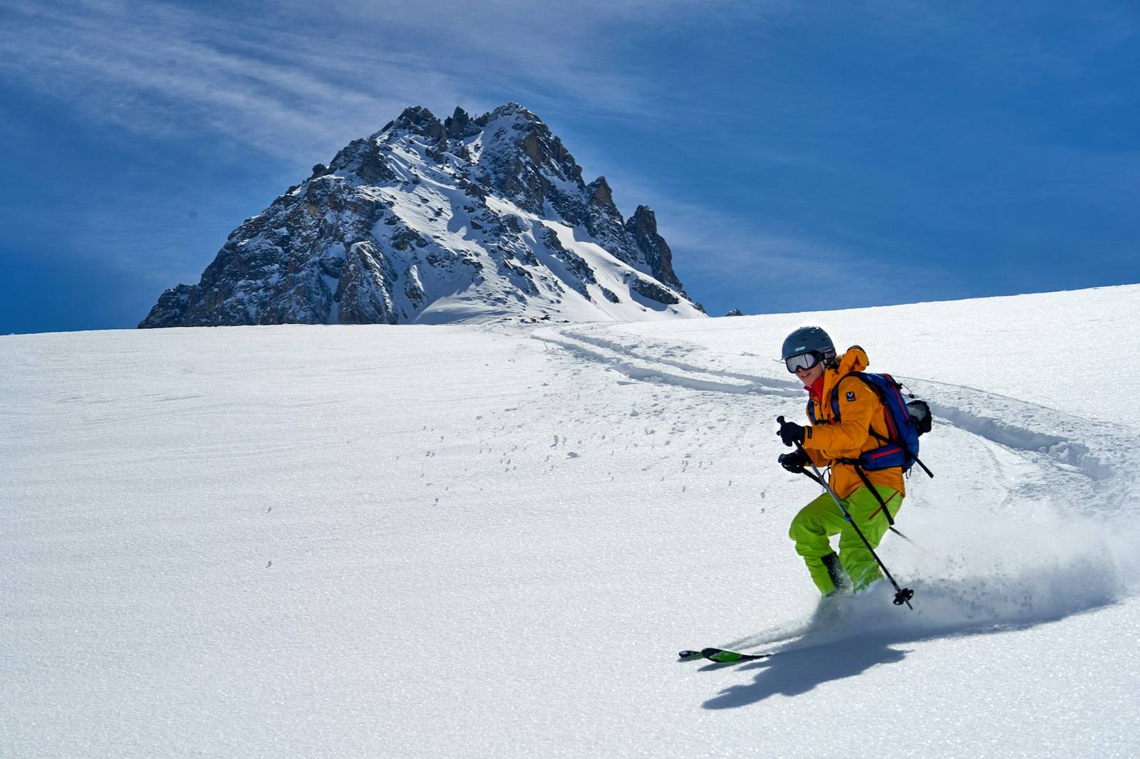 A skier carving through powder below a jagged rocky peak